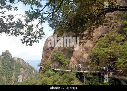 Monte Sanqingshan nella provincia di Jiangxi, Cina. La gente cammina lungo un sentiero aggrappato alla scogliera sul Monte Sanqing. Foto Stock