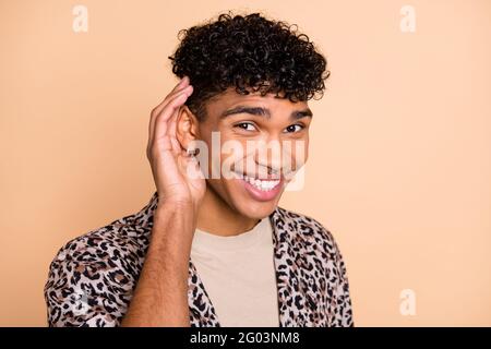 Ritratto di brunet ottimista ragazzo mano orecchio indossare camicia moderna isolato su sfondo di colore beige pastello Foto Stock