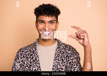 Ritratto di brunet ottimista ragazzo mano mostra piccola usura moderna camicia isolata su sfondo color beige pastello Foto Stock