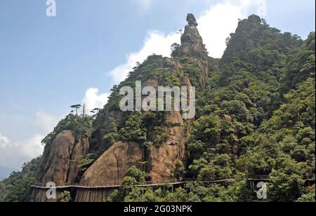 Monte Sanqingshan nella provincia di Jiangxi, Cina. Affioramenti rocciosi e pendii boschivi sul Monte Sanqing. I turisti camminano lungo un sentiero aggrappato alla scogliera Foto Stock