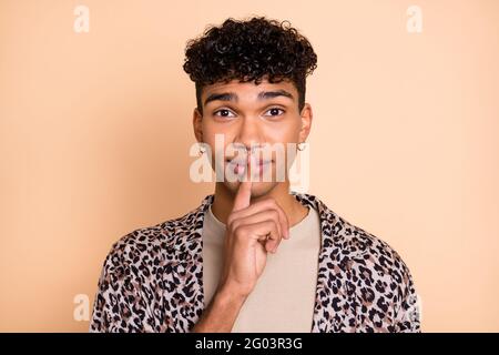 Foto di bel dito di pelle scura che copre bocca labbra non parlare guardare telecamera isolata su sfondo di colore beige Foto Stock
