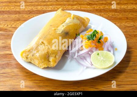 tamale peruviano, tradizionalmente consumato per colazione la domenica, fatto di mais e pollo e servito con salsa criolla - insalata di cipolla. Foto Stock