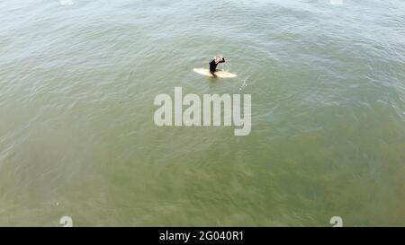 Uomo maturo remare, sdraiato su una tavola da surf - uomo sportivo senior surfing nell'oceano Pacifico, in una giornata di sole con cielo blu e onde trasparenti. Foto Stock