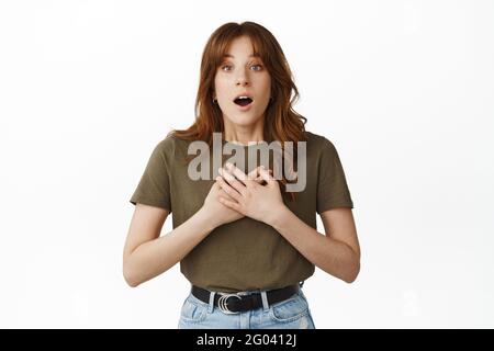 Immagine di una giovane donna sorpresa e toccata, tenere le mani a cuore, gasting in awe, fissando affascinato e stupito dalla pubblicità, sentire notizie sbalorditive Foto Stock