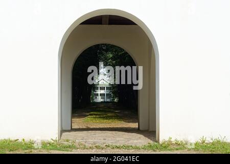 Vista della casa in legno attraverso l'arco del gazebo di osservazione nella tenuta Petrovskoye nel Gory Pushkinskie. Foto Stock