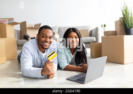 Acquisto di articoli per la casa online concetto. Happy black famiglia che acquista materiale per la loro nuova casa, utilizzando un computer portatile Foto Stock