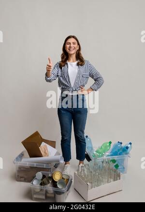 Concetto di sostenibilità. Donna in piedi accanto a contenitori con diversi materiali per il riciclaggio Foto Stock