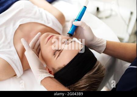 Overhead Rimozione della vista dall'alto della donna che si rilassa durante il massaggio tabella mentre il cosmetologist del medico che esegue peeling dell'aqua sul suo viso per esfoliato e. Foto Stock