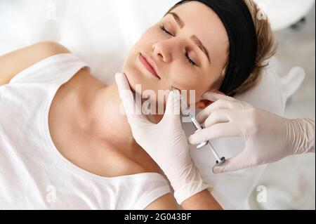 Medico-cosmetologa che fa l'iniezione di bellezza sul volto di una giovane donna al centro di SPA. Concetto di cosmetologia per iniezione per ringiovanimento e correzione Foto Stock
