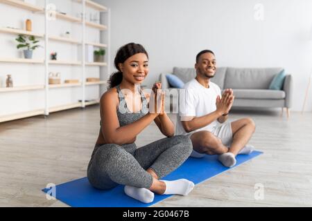 Pratica di yoga domestico durante il covid. Coppia nera meditando o facendo esercizi respiratori, seduto in posa lotus a casa Foto Stock