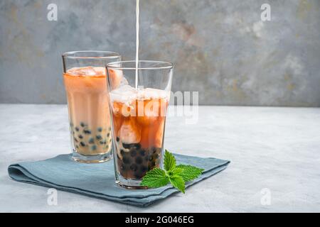 Bubble tea, preparare una bevanda taiwanese con tapioca, latte e ghiaccio su sfondo grigio. Vista laterale. Una bevanda rinfrescante e sana. Foto Stock