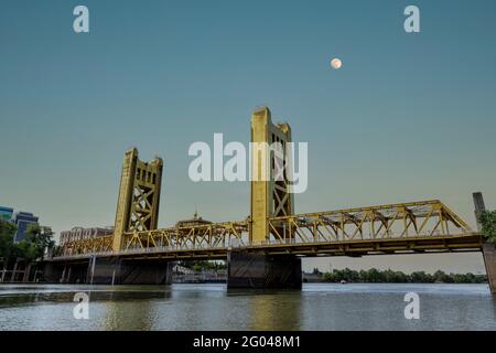 Il Gold Tower Bridge a Sacramento, California. L'ascensore centrale del ponte risalente al 1935 che illumina il sole tramontante con una luna piena visibile. Foto Stock