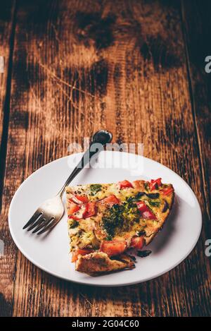Fetta di frittata vegetale con broccoli, peperone rosso e cipolla rossa su piatto bianco Foto Stock
