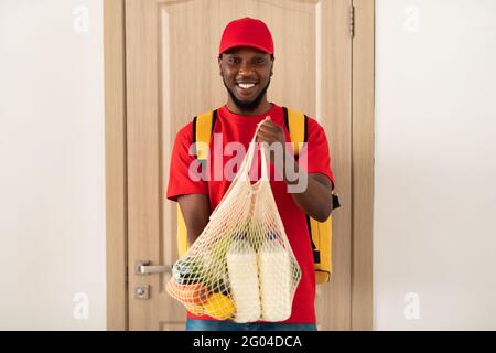 Deliveryman nero che tiene una borsa eco-mesh con generi alimentari Foto Stock