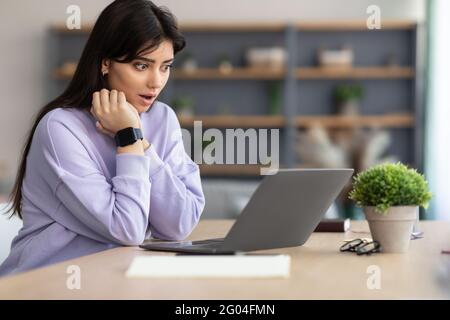 Sorpresa asiatica donna seduta sul divano, utilizzando il computer portatile Foto Stock