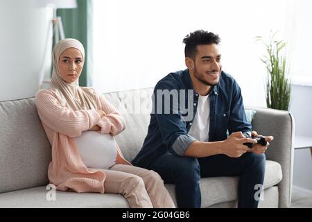 Incinta donna musulmana seduta offesa al marito che giocando Videogiochi Foto Stock