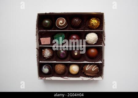 Collezione di cioccolatini belgi di varie forme e sapori in un scatola quadrata isolata su sfondo bianco da un angolo alto visualizza Foto Stock