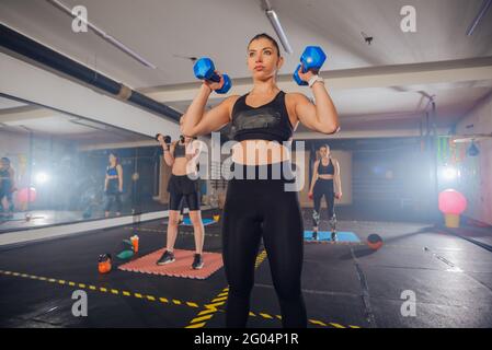 Gruppo di giovani donne atletiche in abbigliamento sportivo con manubri in esercizio in palestra Foto Stock