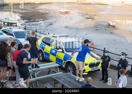 Uomo in cima blu e cappuccio di base palla in piedi sul tavolo da giardino che parla con i poliziotti in maschera di fronte alla macchina di polizia marcata, Margate, Kent, Inghilterra Foto Stock