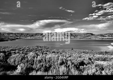 Immagine in scala di grigi di un lago con lunga esposizione circondato da colline sotto un cielo nuvoloso Foto Stock