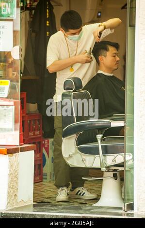 Un barbiere taglia i capelli di un cliente visto attraverso una porta aperta su Danshui Road nel distretto Huangpu di Shanghai, Cina. Foto Stock