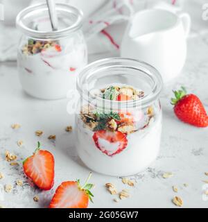 Due vasetti con gustosi parfait di granola, fragole e yogurt su tavola di marmo bianco. Foto Stock