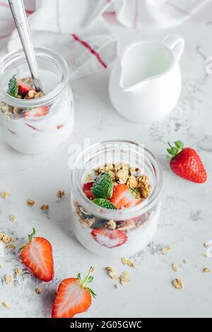 Due vasetti con gustosi parfait di granola, fragole e yogurt su tavola di marmo bianco. Foto Stock