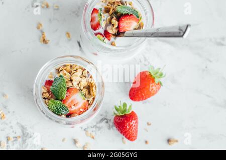 Summet gustosa colazione. Vasetti con parfait in granola, fragole, yogurt su tavola di marmo Foto Stock