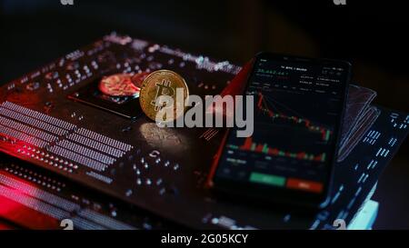 Smartphone con interfaccia cartografica bitcoin e crypto stock su scheda madre illuminata in blu rosso, concetto di finanza e crypto coin Foto Stock