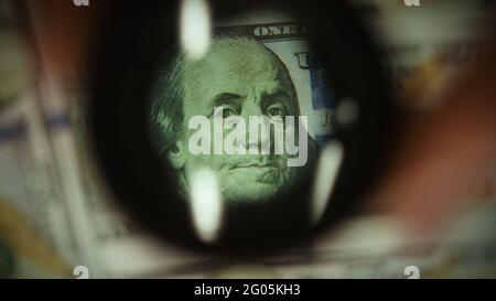 Fronte delle banconote da cento dollari esamina con una lente d'ingrandimento, il concetto di denaro contraffatto e di finanza Foto Stock