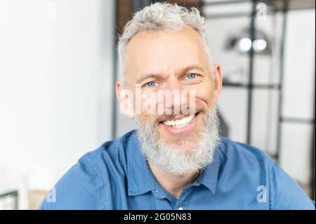 Headshot di bel bel bel bel bell'uomo maturo occhi blu guardando la fotocamera con un sorriso allegro. Primo piano ritratto di un uomo anziano carismatico dai capelli grigi Foto Stock