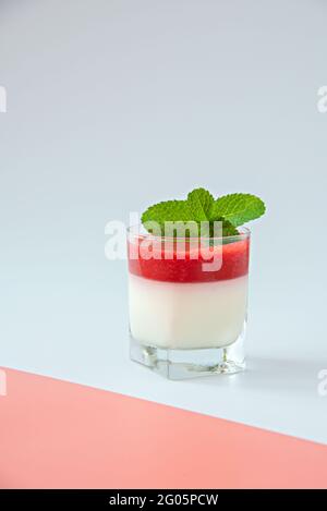 Panna cotta con salsa di fragole in un bicchiere su fondo bianco e rosa. Foto Stock