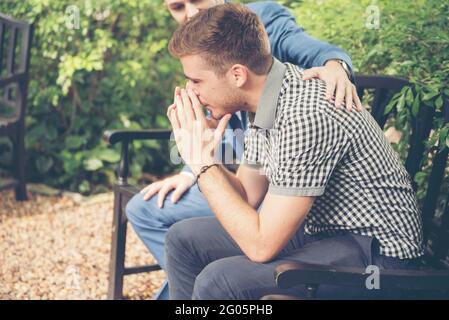 Ragazzi che condividono problemi di vita sempre supportano i migliori amici. Amici che si abbassano cuore rotto. Uomo triste seduto all'aperto nel parco sensazione di tristezza ha una p Foto Stock