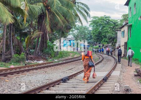 Sri Lanka femmina indossando sari arancio cammina lungo binari ferroviari verso la stazione ferroviaria dopo il lavoro, Colombo, Sri lanka Foto Stock