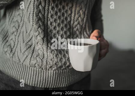 Donna in felpa a maglia grigia calda che tiene tazza di caffè, tè. Concetto di mattina invernale. Foto Stock
