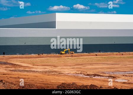 Escavatore solitario accanto a un nuovo magazzino di distribuzione Foto Stock