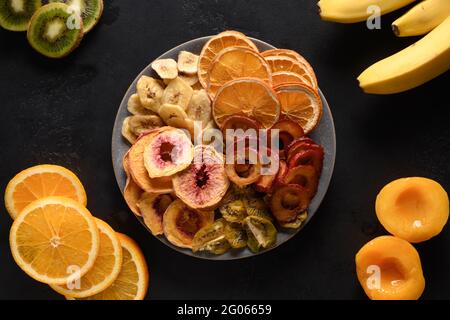 Frutta secca diverse prugne a fette, kiwi, porcini di pesche fondo nero, essiccazione a casa. Snack vegan senza zucchero cibo. Vista dall'alto. Foto Stock