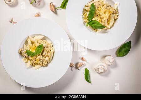 Appetitosa pasta di penne con funghi, salsa cremosa al parmigiano e basilico fresco. Cucina mediterranea tradizionale. Due porzioni su un dorso leggero Foto Stock