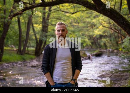 Giovane ragazzo alla moda in posa per una foto in natura con il fiume sullo sfondo Foto Stock