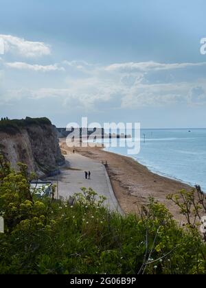 La spazzata di Margate Beach, la scogliera di gesso su un lato, il mare blu increspato verso l'altro con un paio di persone a forma di sagome che camminano lungo il sentiero sulla spiaggia Foto Stock