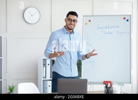 Allegro giovane insegnante arabo in piedi vicino a lavagna e spiegare la grammatica inglese agli studenti online da casa Foto Stock