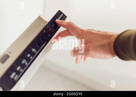 Man premendo il pulsante START sul pannello di controllo della lavastoviglie. Foto Stock
