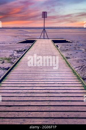 Le tavole di legno di un molo a Lytham in Lancashire, Regno Unito, si estendono sulla spiaggia di sabbia come il sole tramonta creando un cielo drammatico Foto Stock