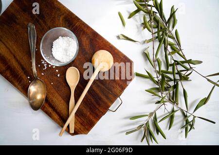 Antico tagliere, sale grosso e piccoli rami d'oliva su fondo bianco di legno, Italia, Europa Foto Stock