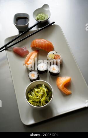 Sushi Set nigiri sashimi e sushi roll su piatto di ceramica serving board con salsa di soia, wasabi, una ciotola di alghe wakame e trissini sopra metallo bac Foto Stock