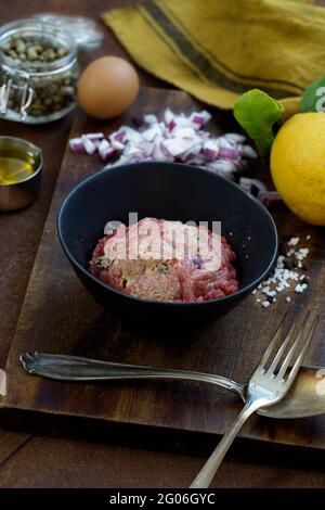 Ingredienti per la preparazione di tartare di manzo su un vecchio tagliere di legno, tessuto da cucina e fondo di metallo arrugginito, Italia, Europa Foto Stock