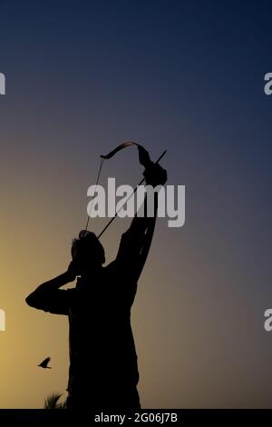 un uomo dalla silhouette che tiene un arco e una freccia davanti al tramonto. Foto Stock