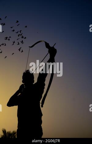 un uomo dalla silhouette che tiene un arco e una freccia davanti al tramonto. Foto Stock