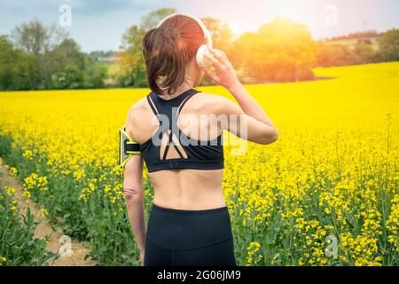 Donna runner sportiva che indossa abiti attivi ascoltando musica con le cuffie mentre si esercita all'esterno in campagna. Concetto di fitness all'aperto. Foto Stock