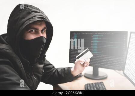 Truffatore hacker in background bianco con carta di credito rubata in mano cerca di rubare denaro dal conto bancario. Concetto di furto di Internet Foto Stock